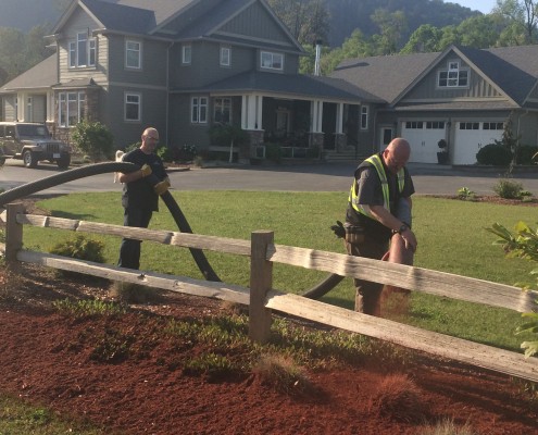 father and son spread landscaping wood chips with blower truck