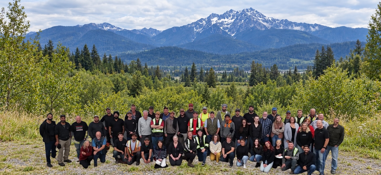 The Denbow team gathered together on a hillside with mountains and forest behind them